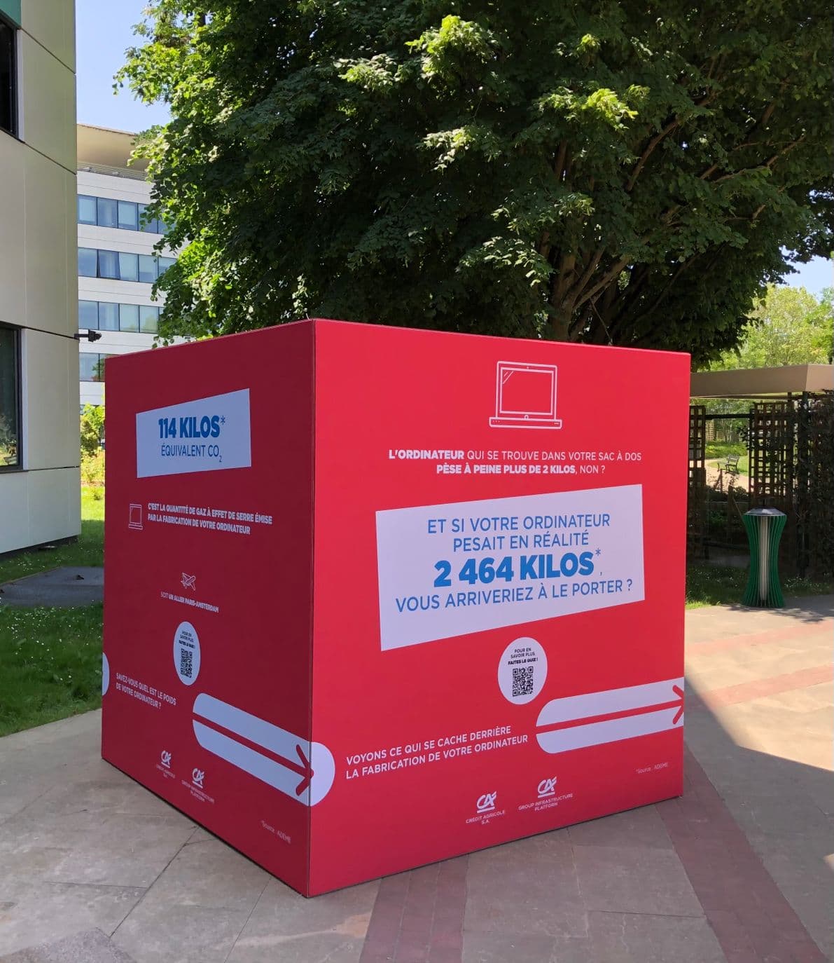 Large red awareness cube set up outdoors, asking whether you would carry your computer if it weighed its real weight of 2,464 kilos