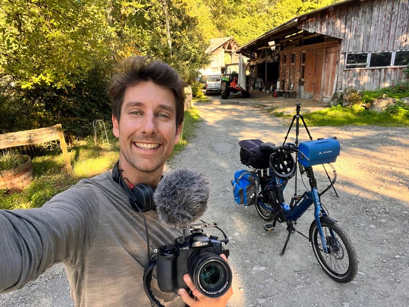 Jérôme Zindy taking a selfie with a camera and a microphone, next to his bike loaded with panniers