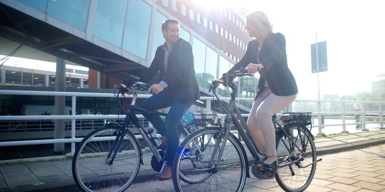 Two colleagues in office clothes riding bikes in the city